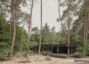 Façade principale intégrée à l'environnement forestier, mettant en valeur l'harmonie entre architecture contemporaine et nature.